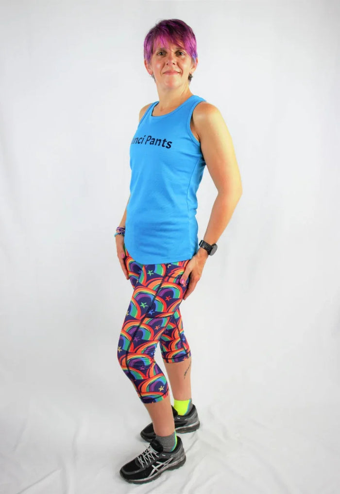 Person with purple hair wearing blue sleeveless top and colorful rainbow star capri leggings in studio