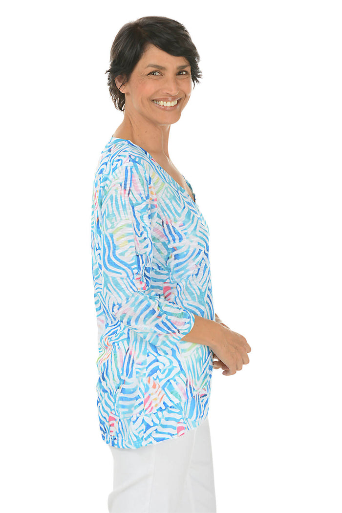 Woman wearing a colorful patterned blouse on a white background. Side shot.