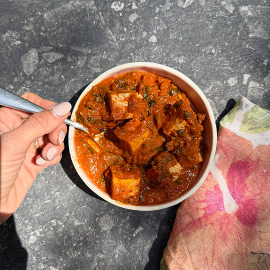 Creamy paneer tikka masala with spinach in a bowl, ready to eat with a fork, on a stone surface beside a floral napkin.