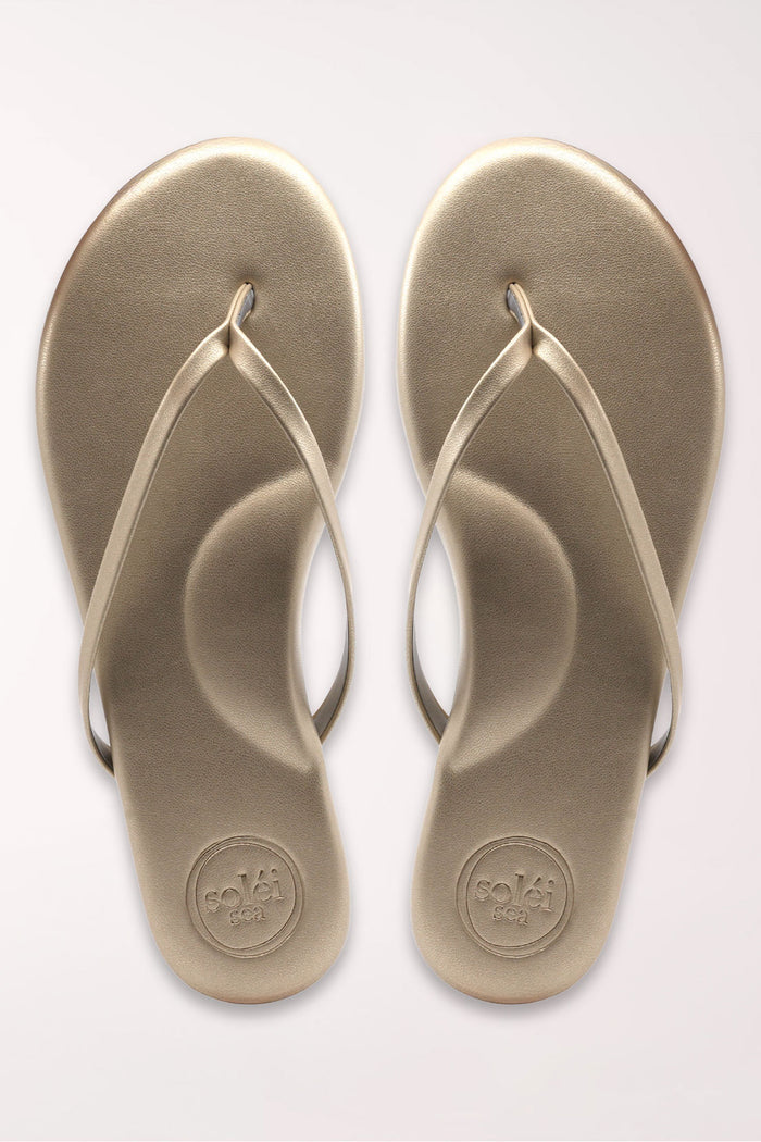 Pair of champagne gold flip-flops on a white background