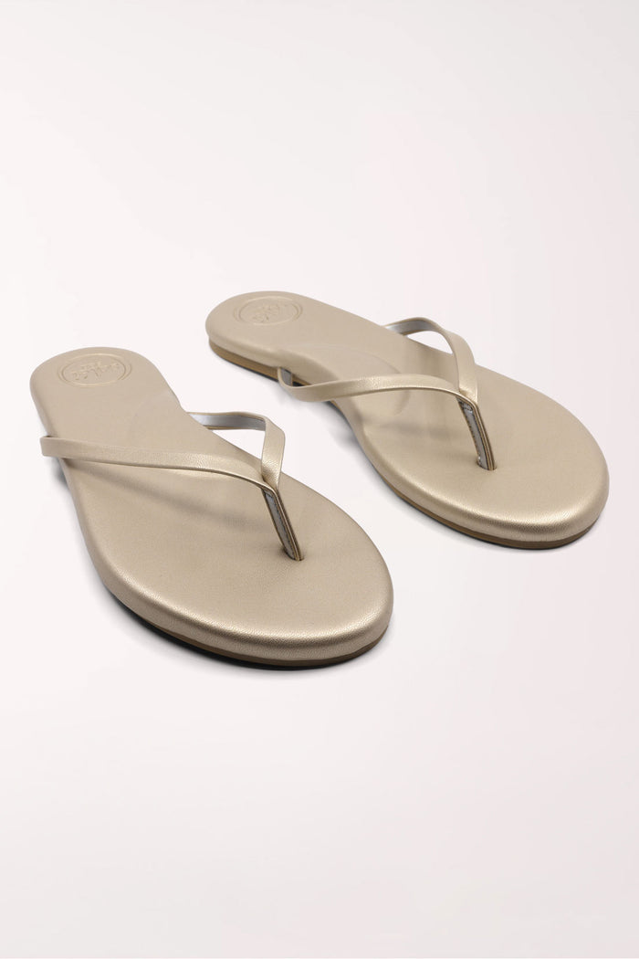 Pair of champagne gold flip-flops on a white background