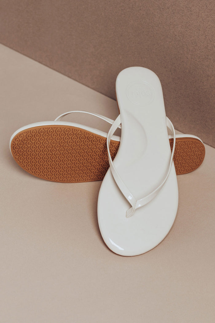 White flip-flop sandal with brown sole on a beige surface
