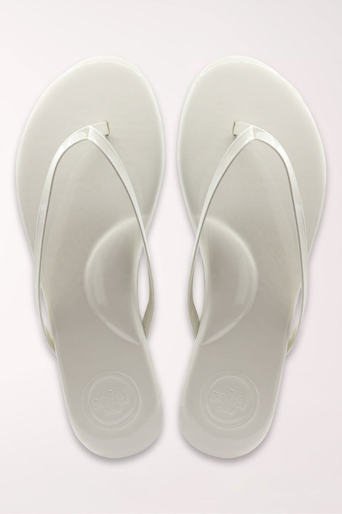 White flip-flop sandal with brown sole on a beige surface