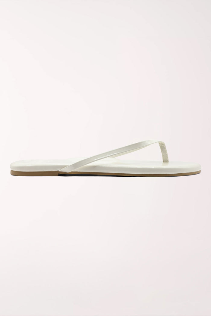 White flip-flop sandal with brown sole on a beige surface