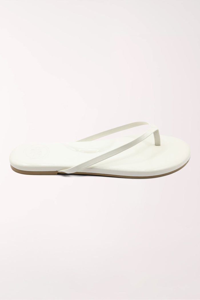 White flip-flop sandal with brown sole on a beige surface