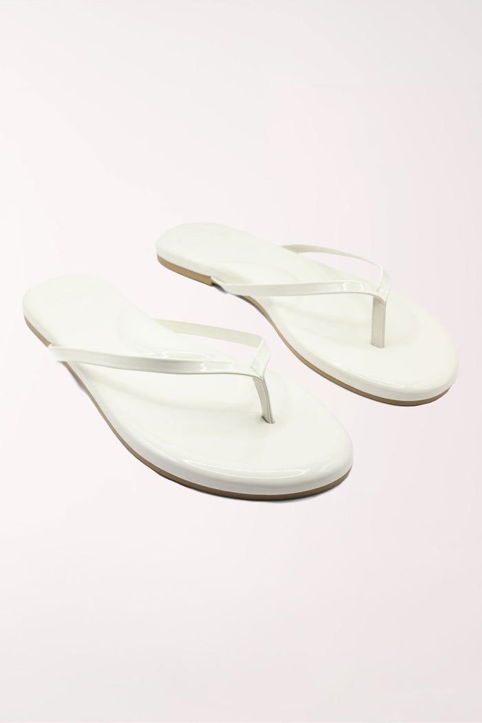 White flip-flop sandal with brown sole on a beige surface