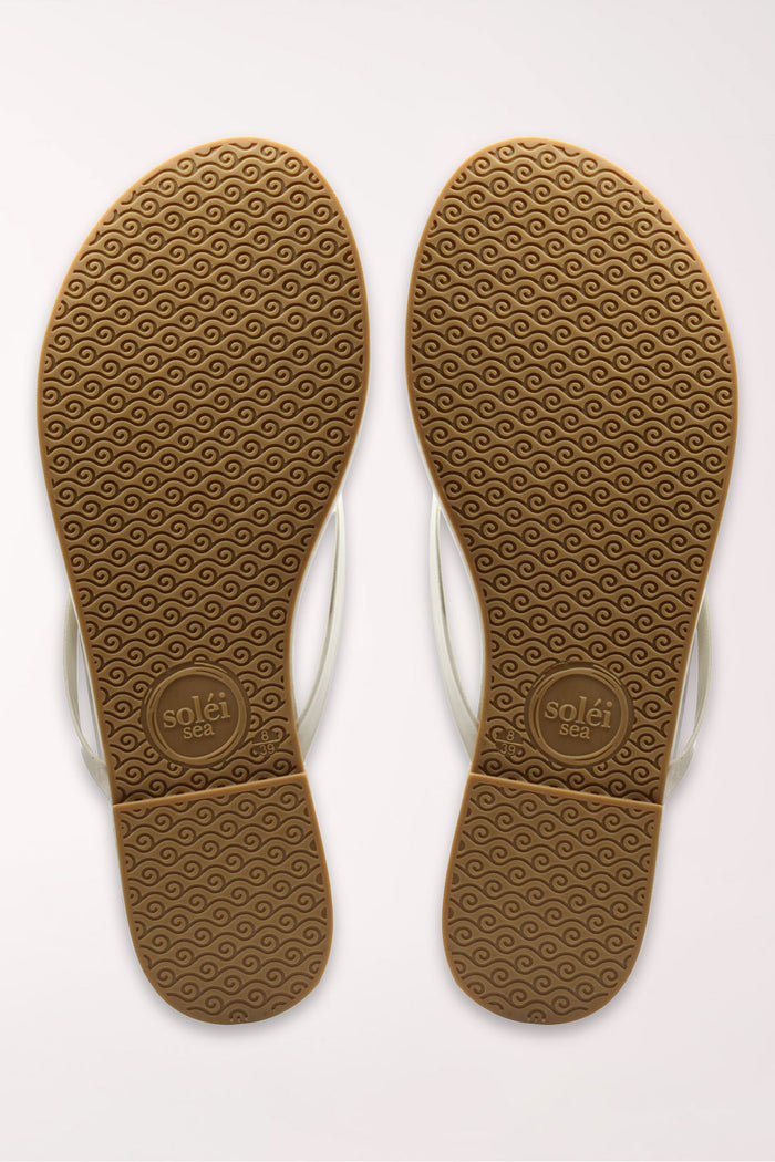 White flip-flop sandal with brown sole on a beige surface