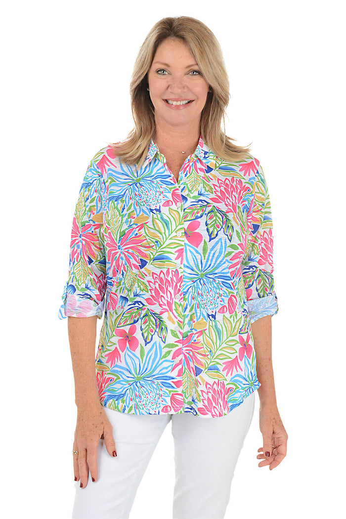 Woman wearing a colorful floral blouse with white pants on a white background.