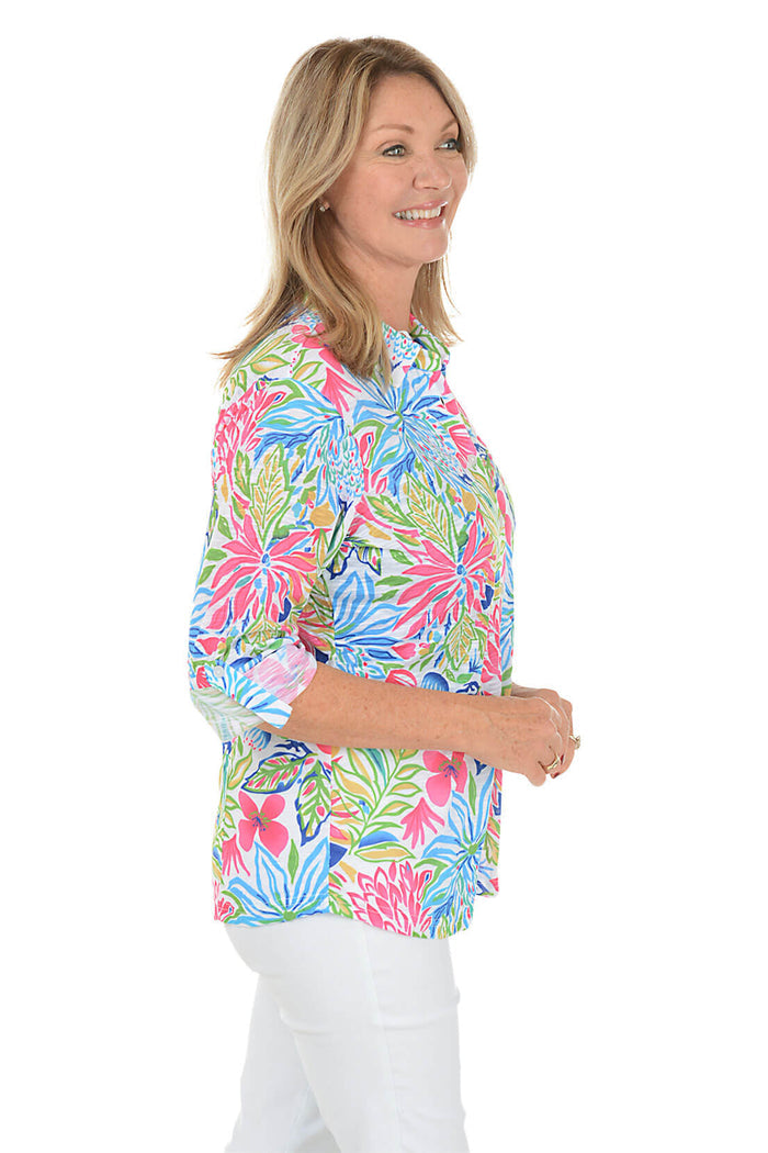 Woman wearing a colorful floral blouse with white pants on a white background. Side shot.