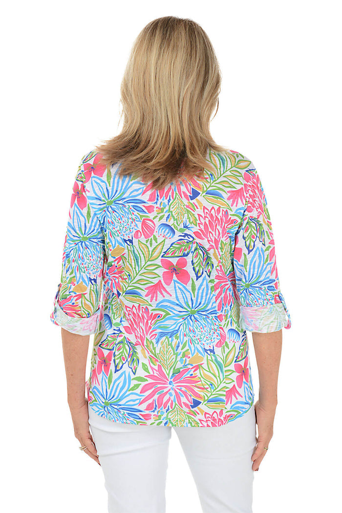 Woman wearing a colorful floral blouse with white pants on a white background. Back shot.