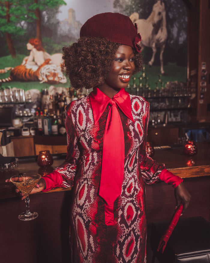 Woman in a stylish red and patterned outfit with a red tie in a bar setting.
