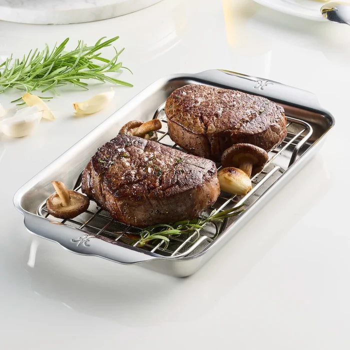 Two grilled steaks on a metal grill pan with herbs and garlic on a white surface