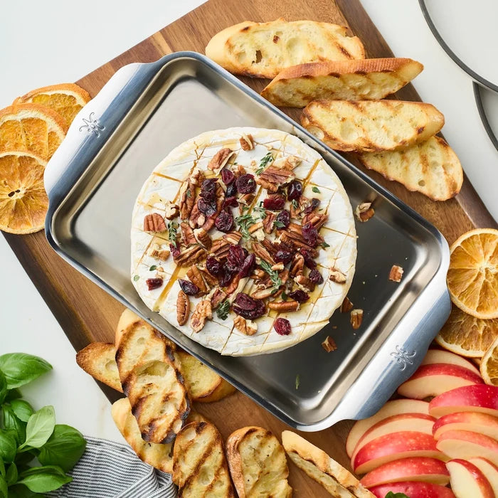 Baked brie with cranberries and pecans on a metal tray with crostini and apples.