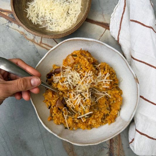 Creamy pumpkin risotto with grated cheese, served in a rustic bowl with a spoon, ready to eat.