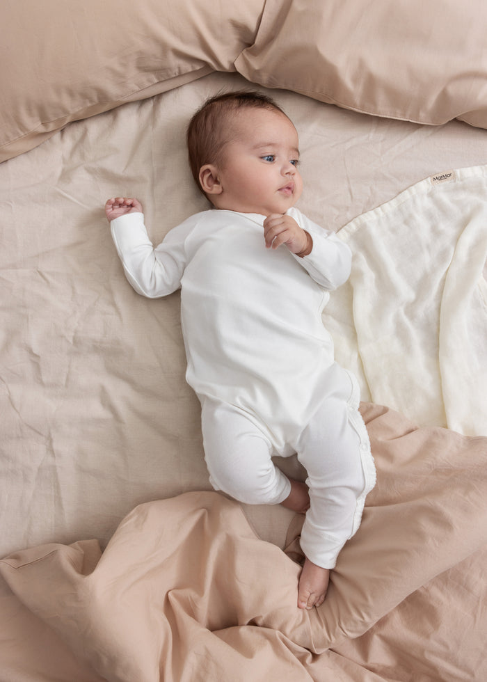 Baby wearing beige/grey knitted set lying in wicker basket with beige blanket.