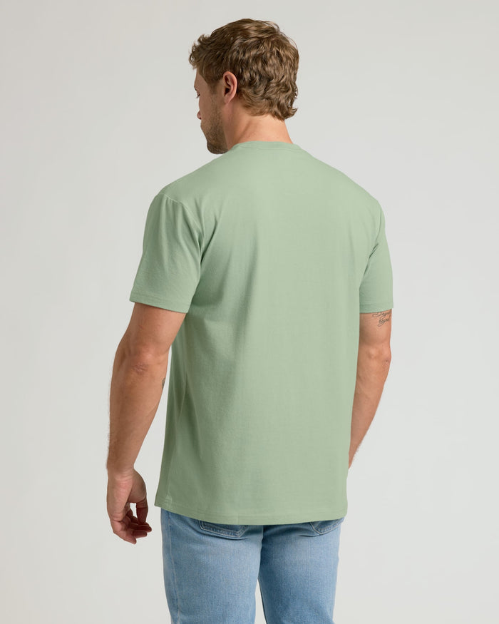 Man wearing a light green t-shirt and blue jeans on a plain background